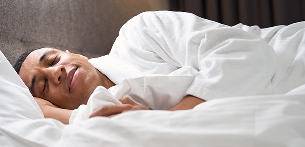 man sleeping comfortably in a white robe in bed showing relaxed and peaceful sleep for better rest and health three benefits of sleep